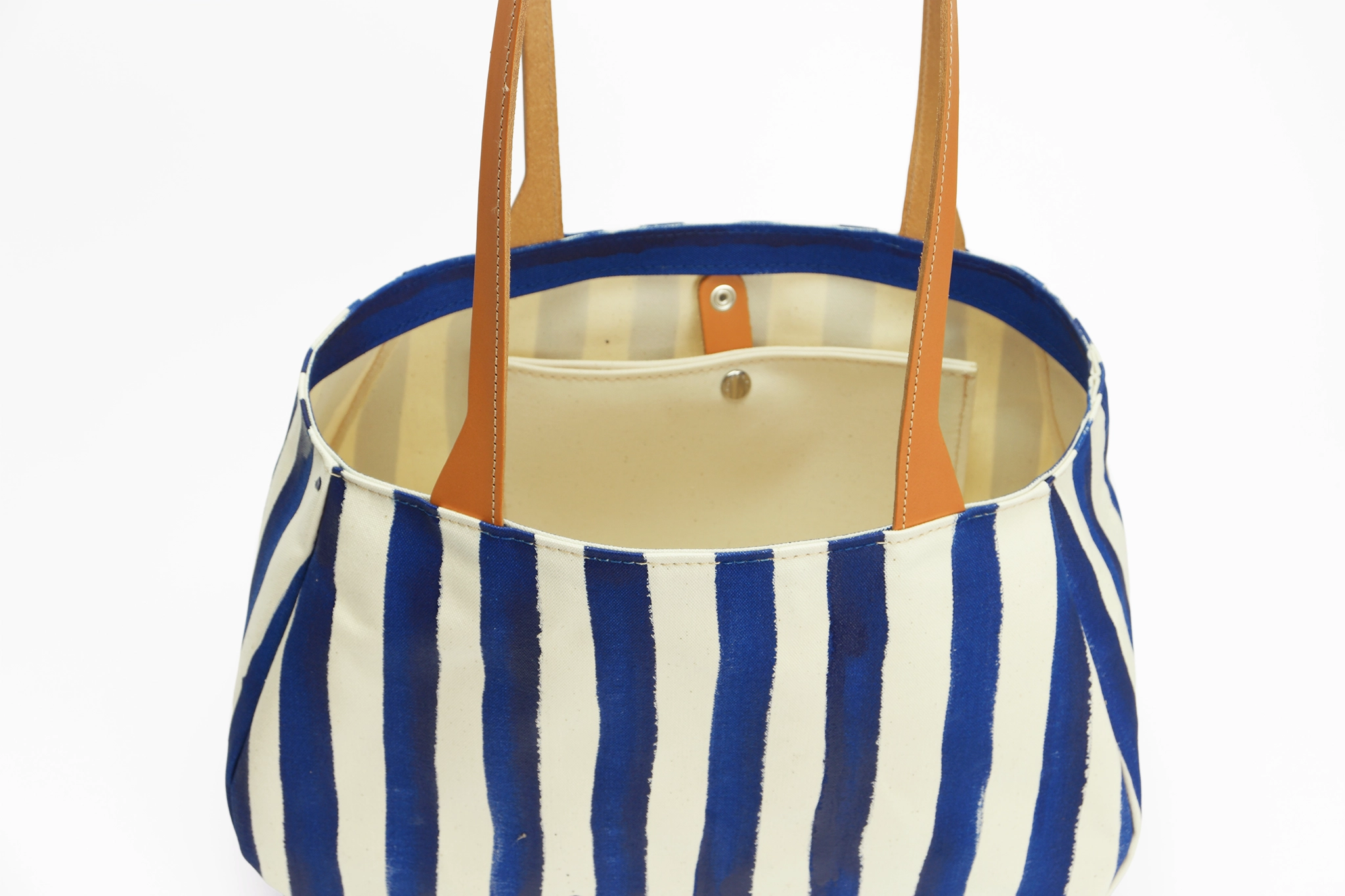 Vue du dessus ouvert du sac cabas fourre-tout en toile et cuir - Rayé bleu et blanc. Anse en cuir marron. Et pochette intérieure déclipsable.